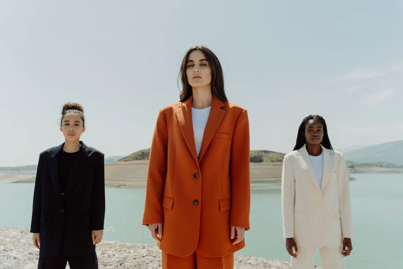 An orange tailored suit framed by dark and ivory silhouettes against an open landscape.