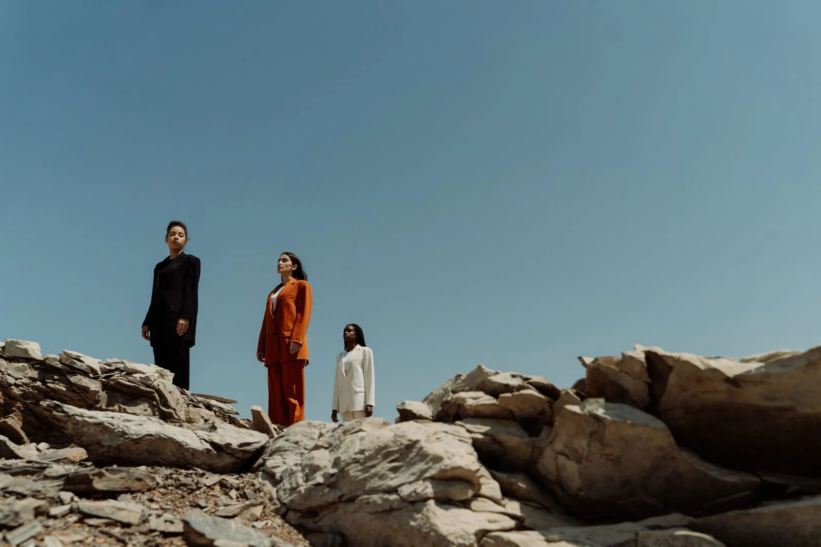 Three tailored silhouettes in black, orange and ivory on a rocky hillside under a blue sky.