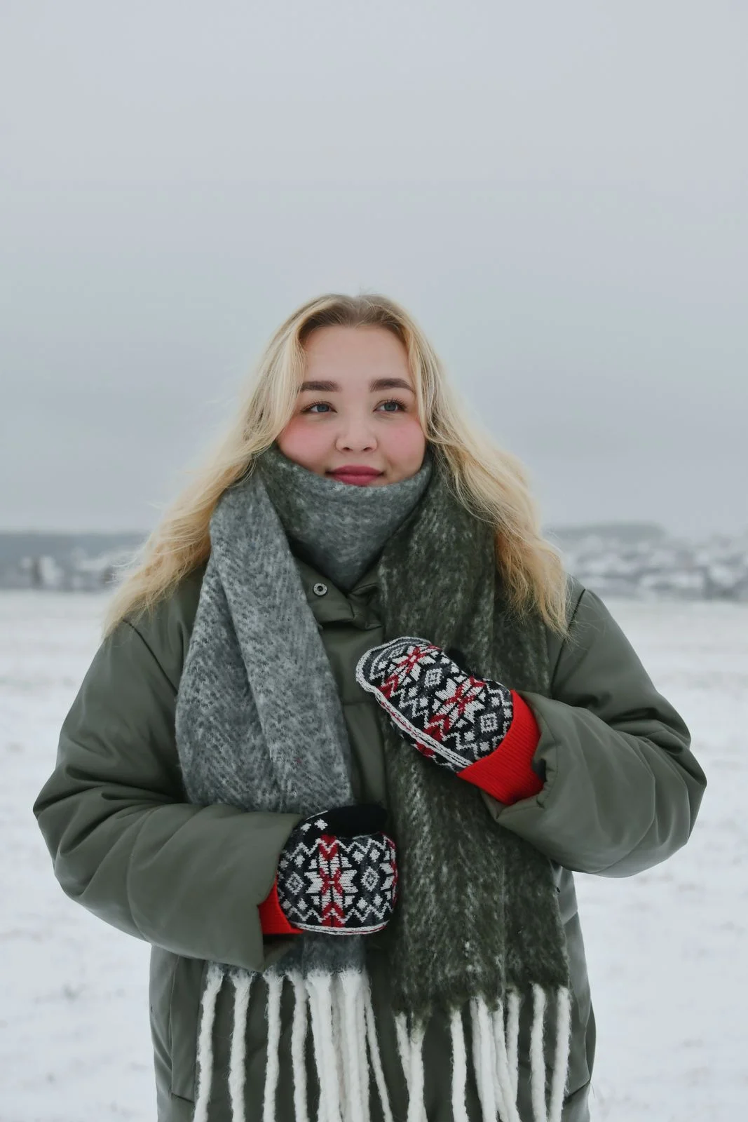 Black, white and red patterned knitted mittens, photographed on hands outdoors.