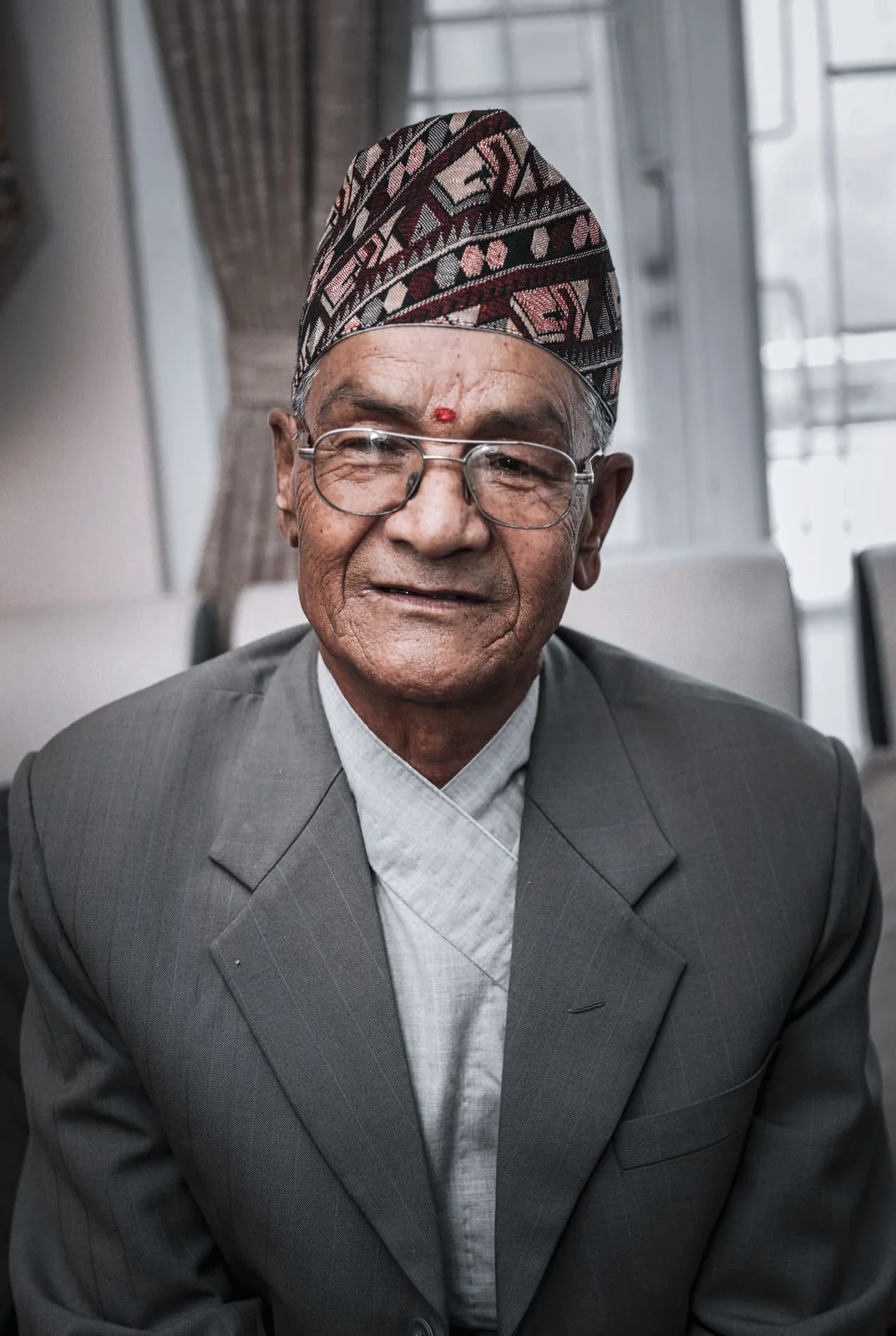 Maroon, pink and black patterned topi shown worn with a jacket.