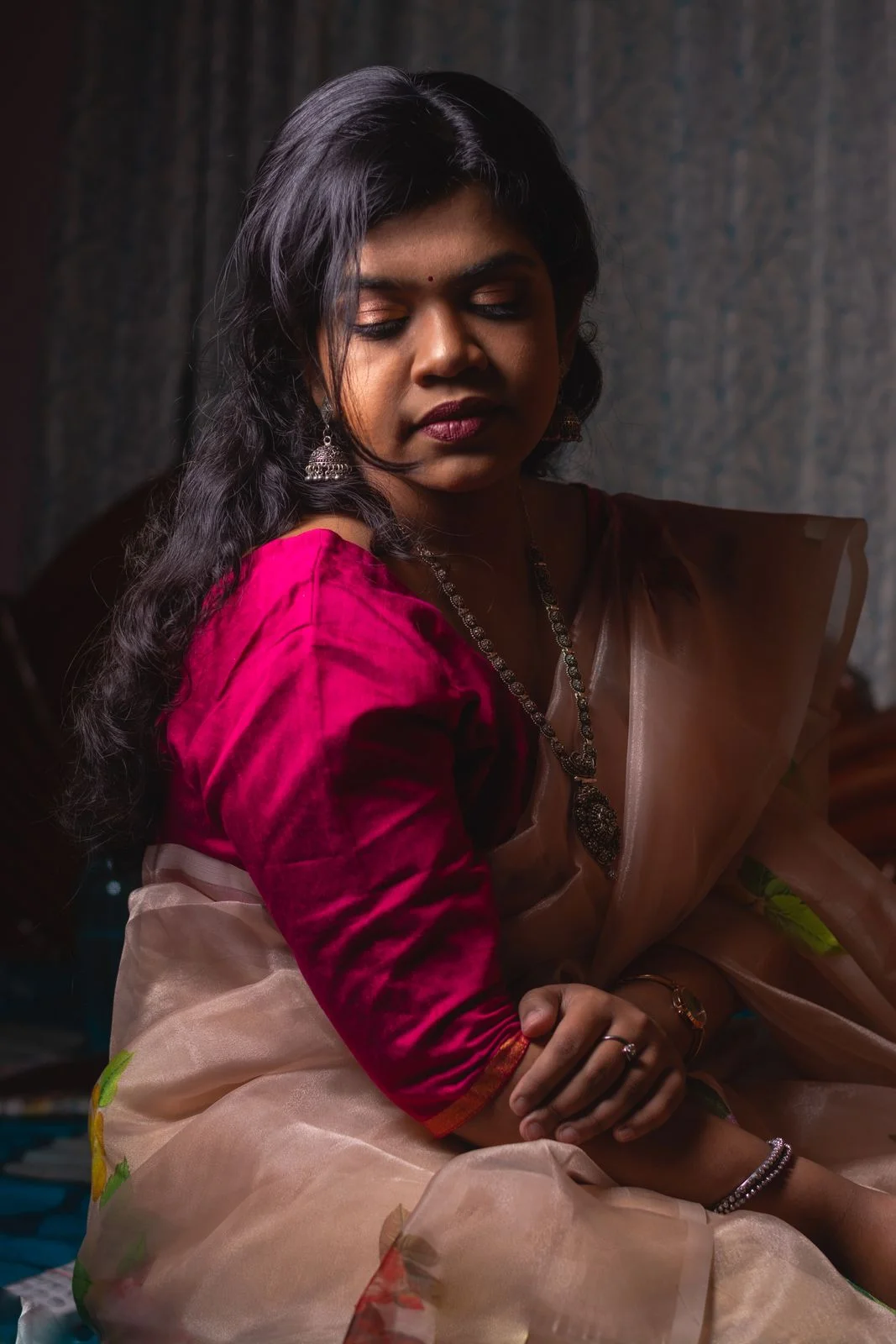 Magenta sari blouse with gold-tone cuff trim, seated side view.